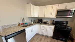 A kitchen with white cabinets, a stainless steel dishwasher, a black stove, and a microwave. - Historic Home | Walk to Lake & Strip Fun (Geneva)