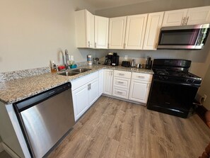 A kitchen with white cabinets, a stainless steel dishwasher, a black stove, and a microwave.
