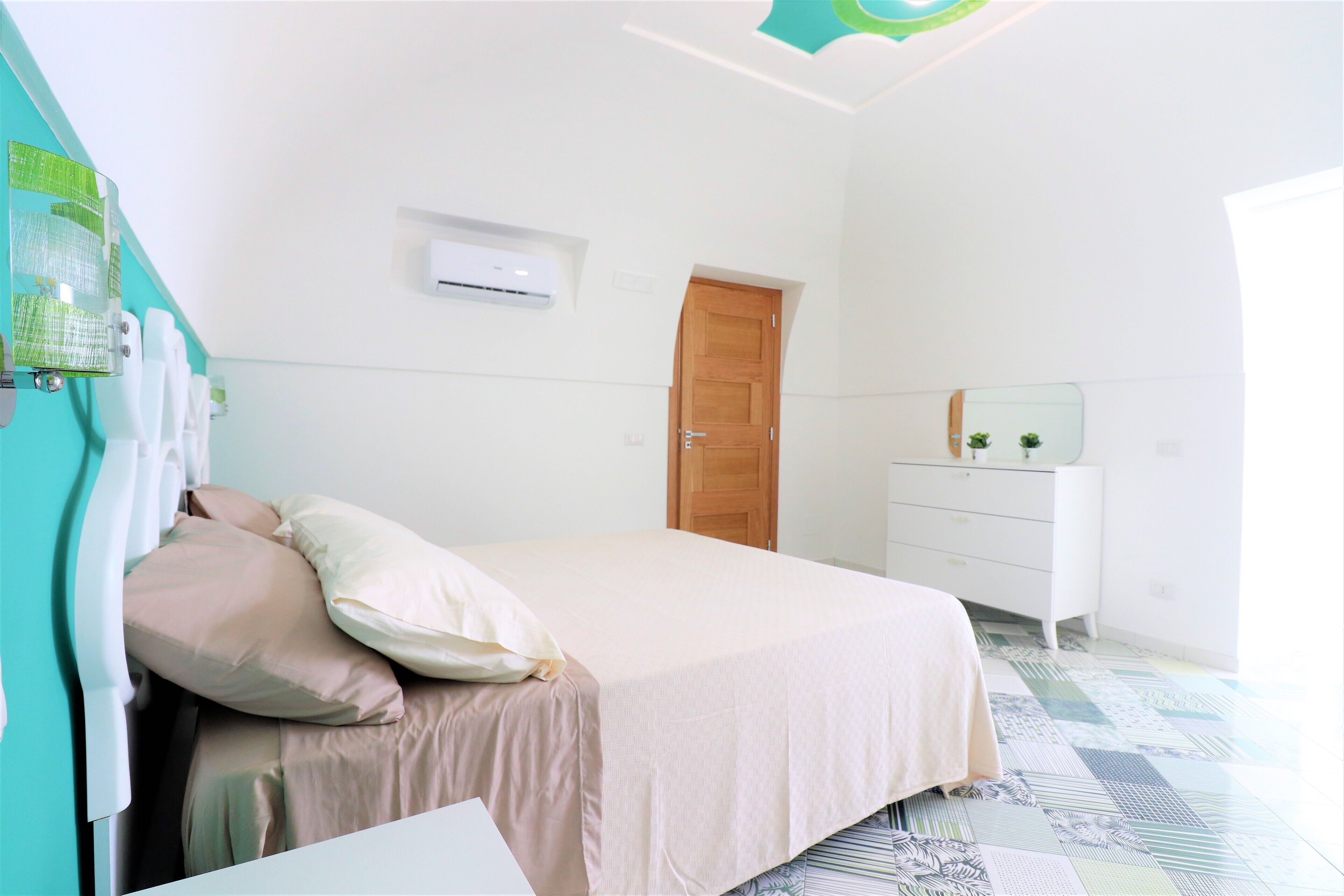 Ein Schlafzimmer mit Bett, Schminktisch, Tür und Wandgerät zur Klimatisierung.