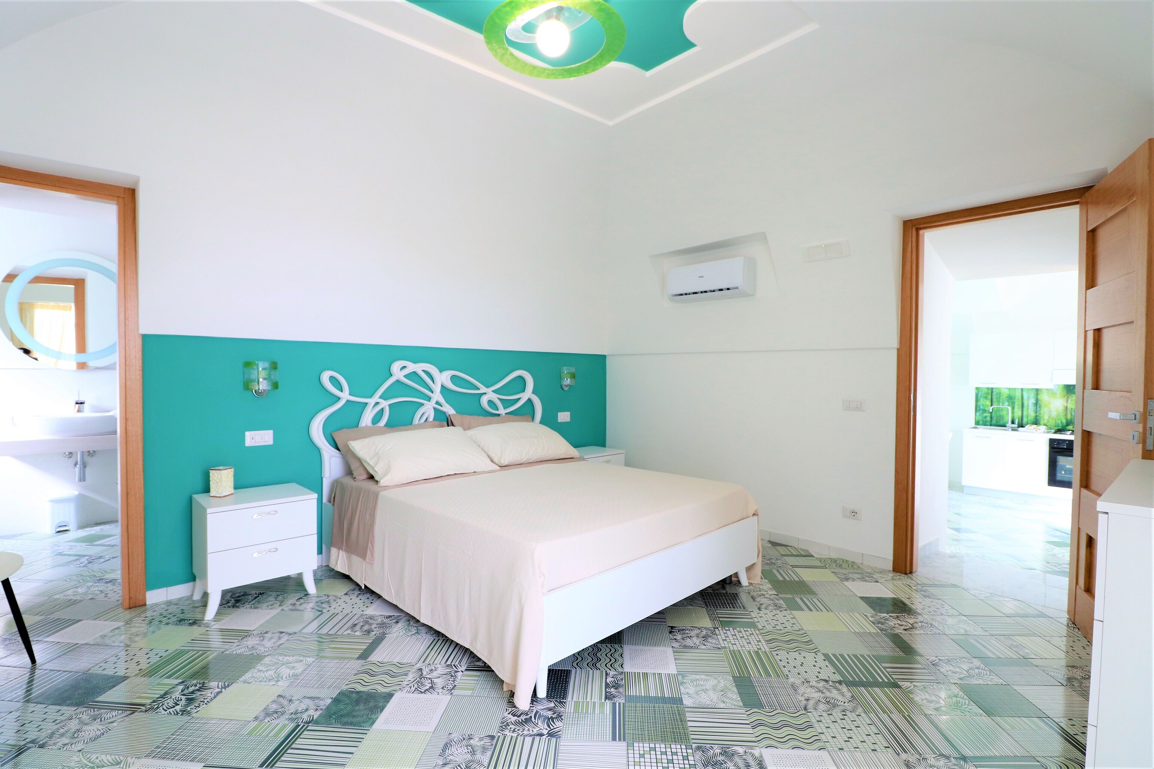 Un dormitorio con cama, mesita de noche y baño visible a través de una puerta abierta.