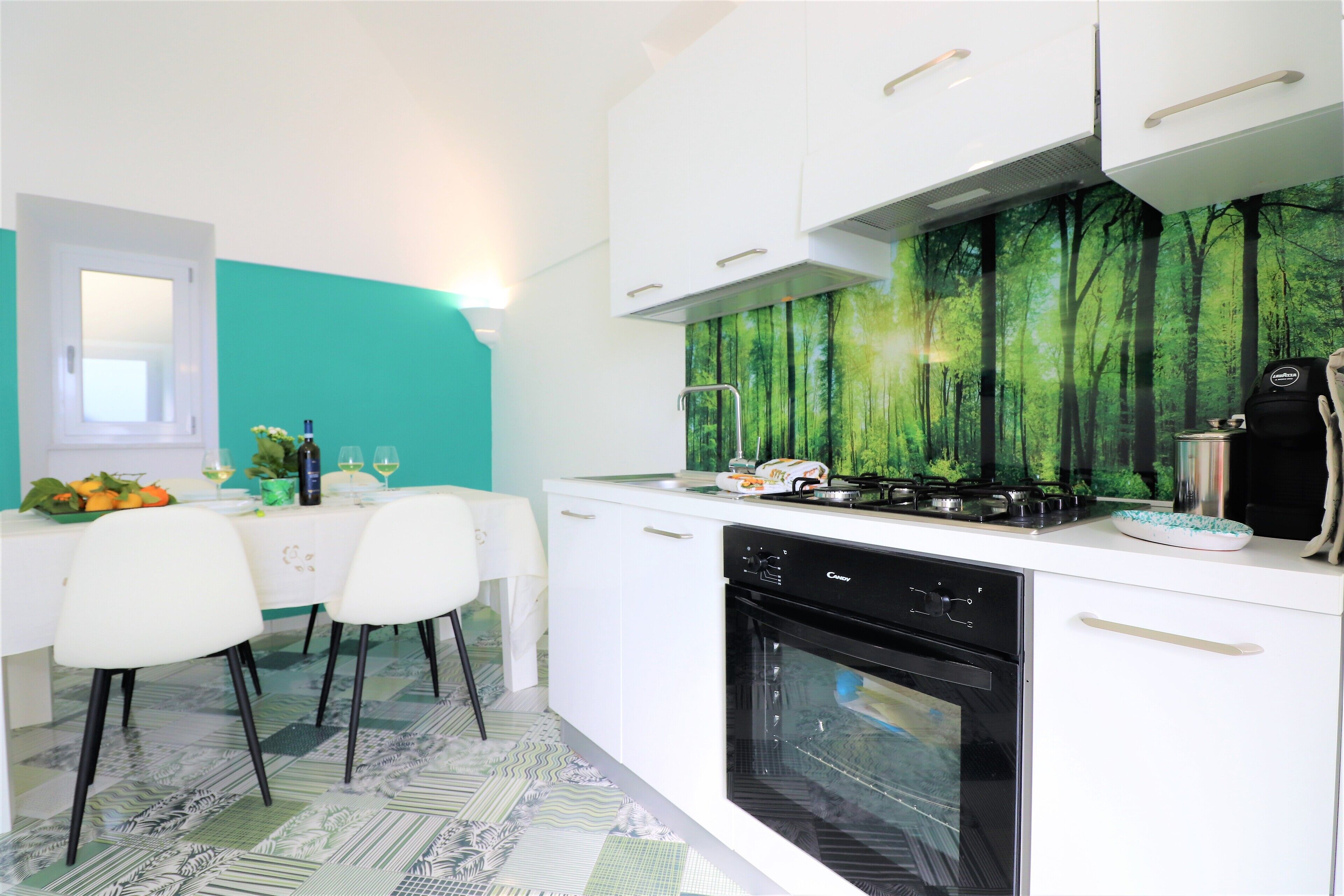 Una cocina moderna con armarios blancos, un lavavajillas negro y un salpicadero decorado con motivos forestales.
