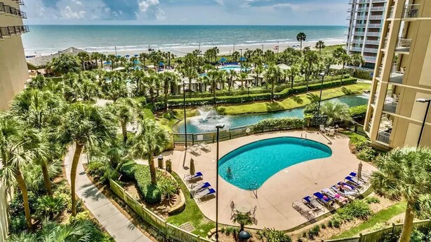 A resort with a large pool, palm trees, and a view of the ocean.