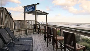 A wooden deck with lounge chairs and a sign indicating beach access.