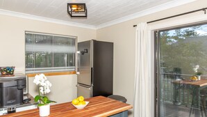 A kitchen with a wooden table, a refrigerator, a coffee maker, and a window with blinds.