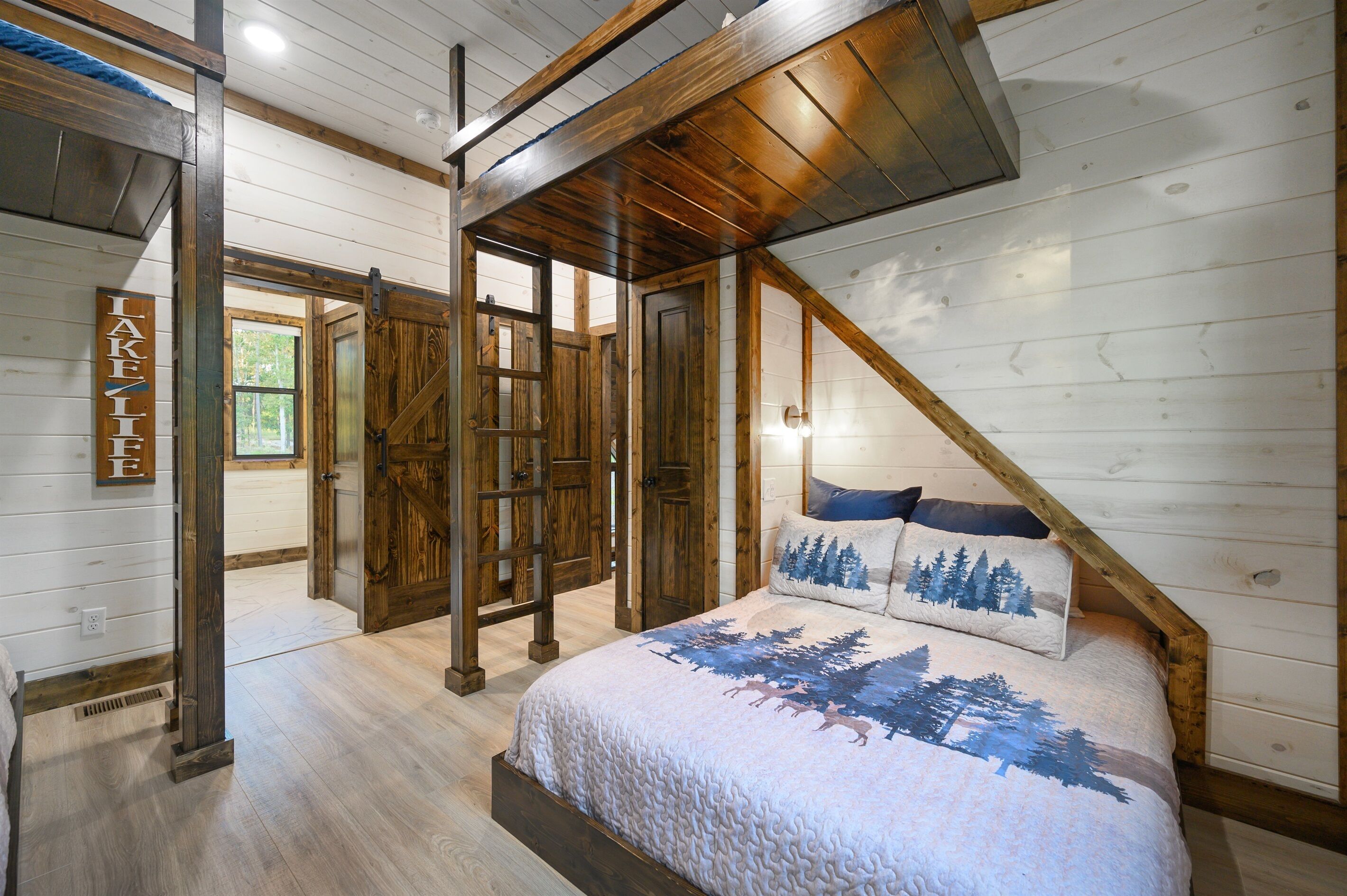 A bedroom with a wooden ceiling, a bed with a forest-themed bedspread, and a sign that reads "LAKE".