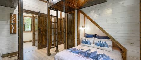 A bedroom with a wooden ceiling, a bed with a forest-themed bedspread, and a sign that reads "LAKE".