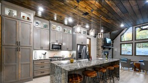 A modern kitchen with granite countertops, stainless steel appliances, and a large island with bar stools. - Lux Cabin Private Pond Cust Playset 1 Mile to Lake Cvrd Deck+Entmt Amenities (Broken Bow)