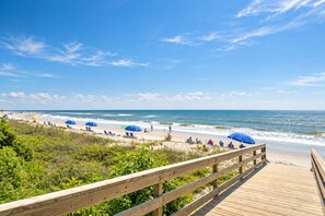 A wooden boardwalk leading to a beach with umbrellas and people.