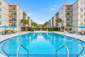 Une piscine entourée d’un bâtiment doté de balcons, de palmiers et d’un espace salon extérieur.