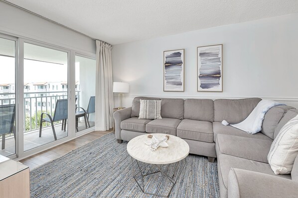 A modern living room with a grey sofa, a round coffee table, and a view of a balcony with a chair.