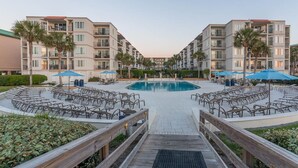 Un hotel con piscina central rodeada de zonas de estar al aire libre y palmeras.