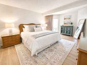 Ein Schlafzimmer mit Bett, Nachttischen, Kommode, Schrank und einem Fenster mit Vorhängen.