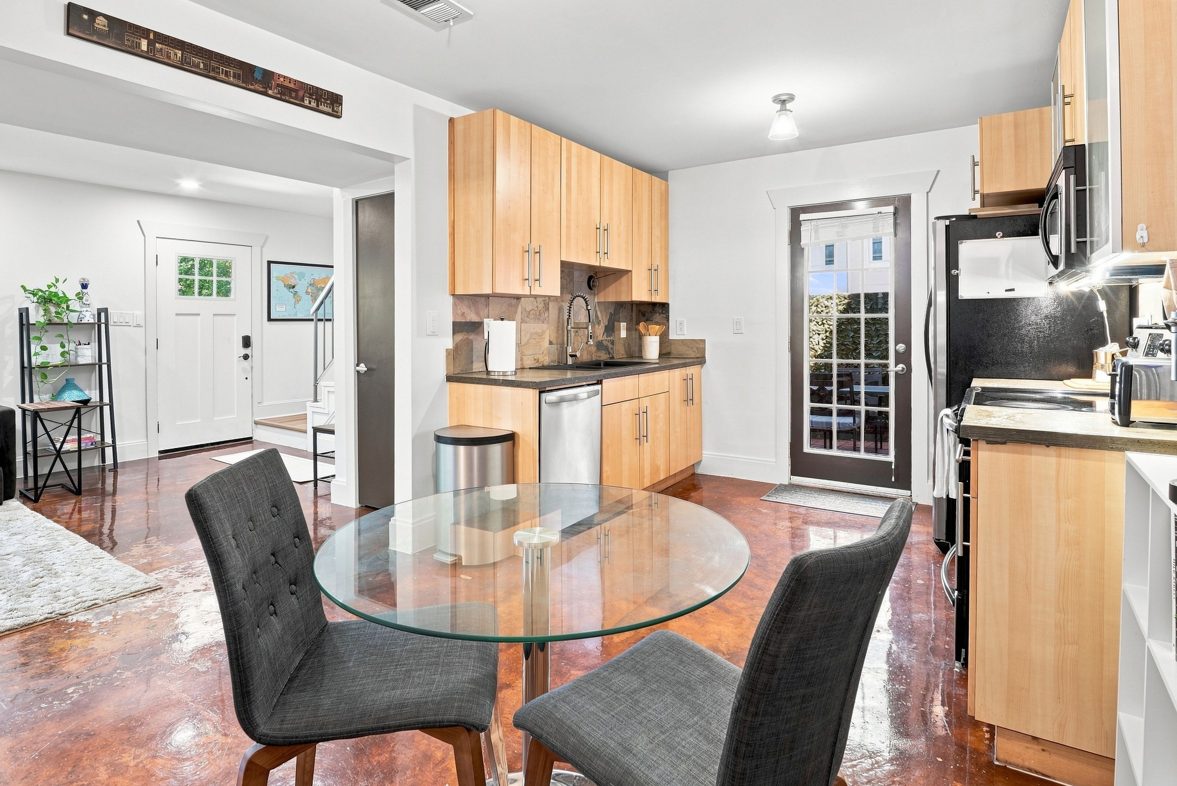A modern kitchen with wooden cabinets, a glass dining table, and a stainless steel refrigerator.