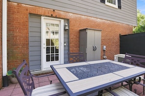 Une terrasse avec une table et des chaises, une porte et un petit abri de jardin gris.