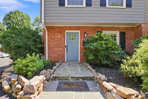 A two-story house with a grey siding exterior, a blue front door, and a stone pathway leading to the entrance.