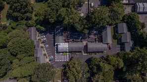 Une vue aérienne d’un parking où sont garées plusieurs voitures, entouré d’une végétation luxuriante et de bâtiments.