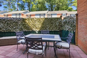 Une terrasse avec une table et des chaises, un mur en briques et une haie.