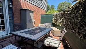 Un'area patio con tavolo e sedie, un muro in mattoni e un siepe verde.