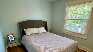 Una camera da letto con un letto, un comodino, una finestra con persiane e una ventola a soffitto.