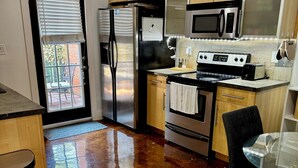 Una cucina con mobili in legno, elettrodomestici in acciaio inossidabile, un tavolo in vetro e una sedia nera.