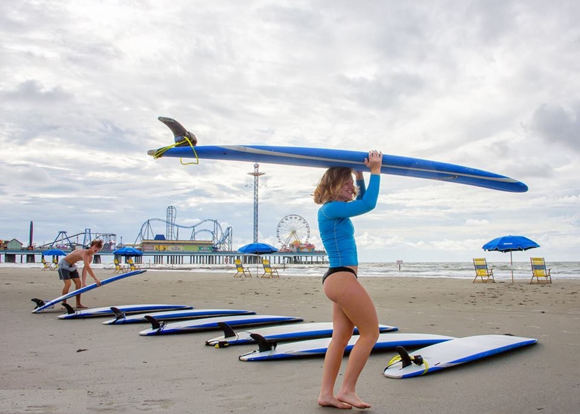 Una playa con tablas de surf alineadas y una noria al fondo.