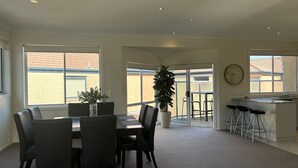 Un vaste espace dédié à la salle à manger, avec une grande table et des chaises, une plante en pot, et une vue sur une terrasse extérieure, accessible par une porte vitrée.