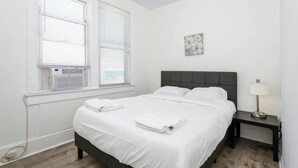 A bedroom with a bed, bedside table, lamp, and artwork on the wall. - Modern Beachfront Suite 304 (Ocean City)