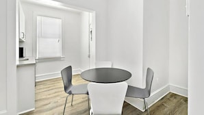A modern room with a round table, two chairs, a window with blinds, and a door. - Modern Beachfront Suite 304 (Ocean City)