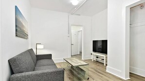 A modern living room with a grey sofa, a glass coffee table, a flat-screen TV, and a door leading to another room. - Modern Beachfront Suite 304 (Ocean City)