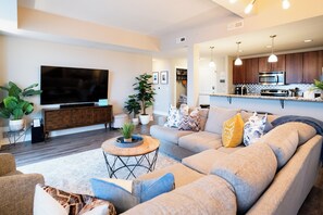A modern living room with a large flat-screen TV, a sofa, and a coffee table. - Spacious 3 BR 2 Bath Loft Condo in Grand Landing (Grand Haven)