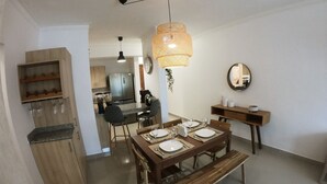 Een eetgedeelte met een houten tafel gedekt voor vier personen, een bankje en een keuken op de achtergrond.