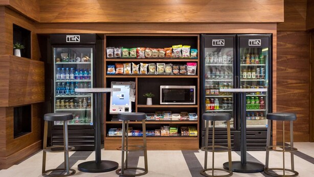 Een moderne ontspanningsruimte met automaten, planken vol snacks en drankjes, en een digitaal kiosk.
