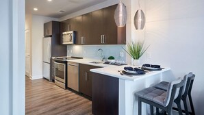 A modern kitchen with dark cabinetry, stainless steel appliances, and a central island with seating. - Global Luxury Suites Clarendon Metro (Arlington)