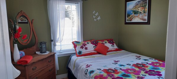 Quarto com cama, cómoda, espelho, janela com persianas e um quadro pendurado na parede.