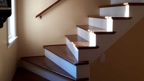 Eine Treppe mit Holzstufen und Geländer, die zu einer Zwischenebene mit Lichtschalter führt.