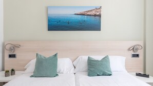 Ett hotellrum med en säng, två kuddar, en tavla som hänger på väggen och föreställer en strand, och sänglampor.