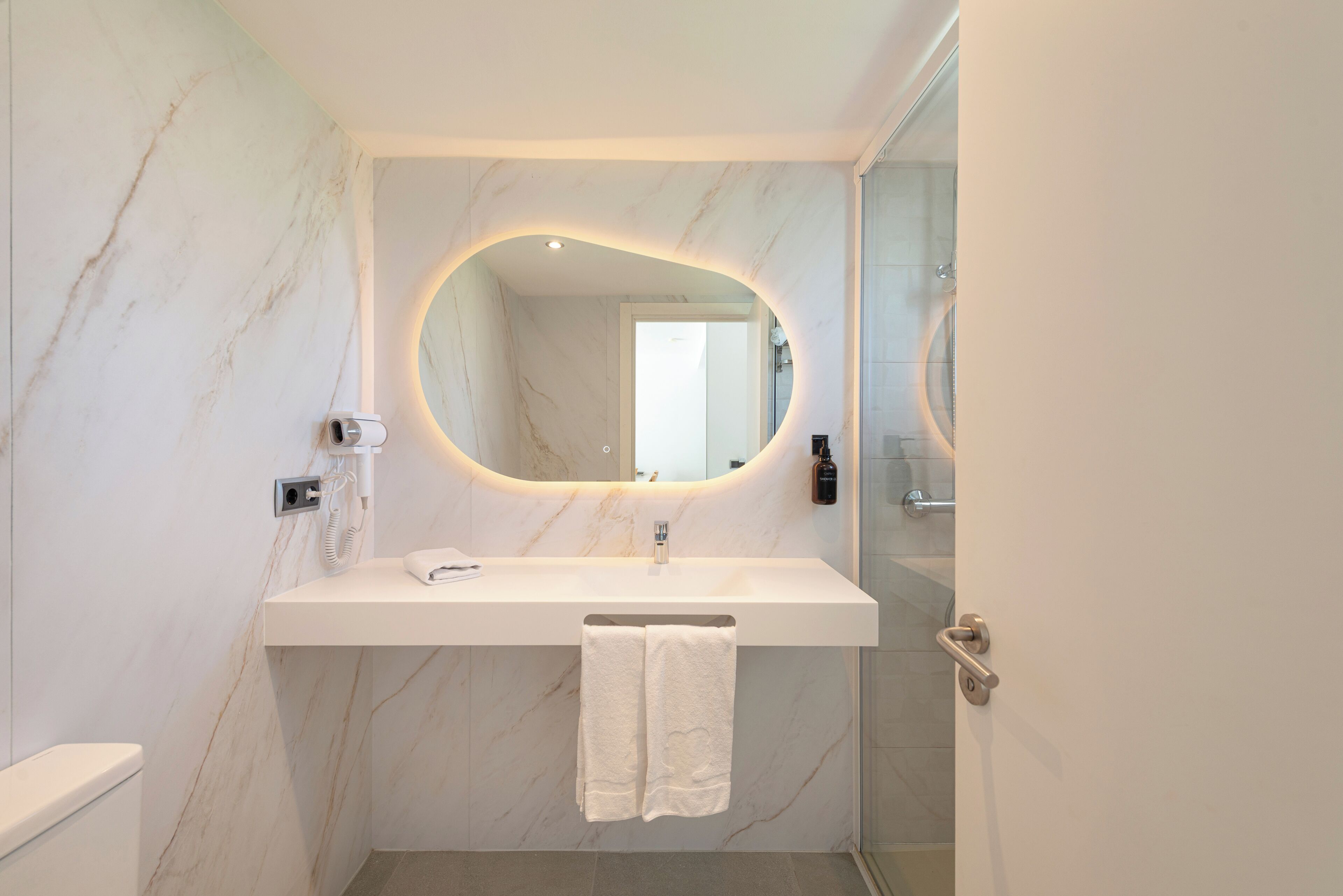 A bathroom with a marble wall, a white sink, a mirror, and a towel rack.