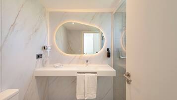 A bathroom with a marble wall, a white sink, a mirror, and a towel rack.