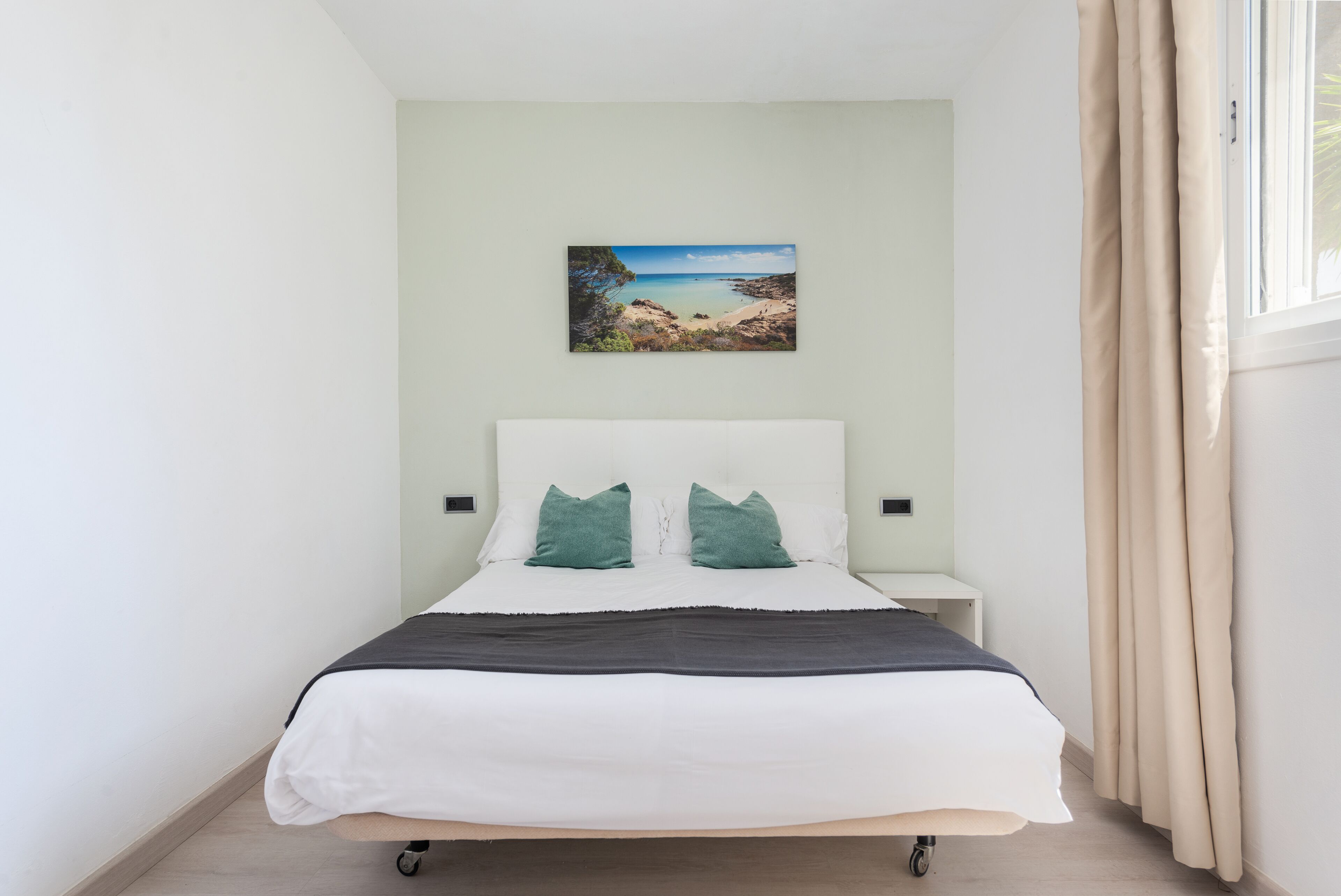 A neatly arranged bedroom with a bed, a nightstand, a wall-mounted painting, and a window with curtains.