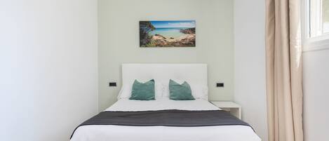 A neatly arranged bedroom with a bed, a nightstand, a wall-mounted painting, and a window with curtains.