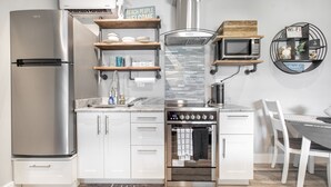 Eine moderne Küche mit Edelstahl-Kühlschrank, Backofen und Mikrowelle. Über der Arbeitsfläche befinden sich Holzregale und ein Schild mit der Aufschrift 'Beach People Welcome'.