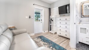 Ein modernes Wohnzimmer mit einem weißen Sofa, einem an der Wand befestigten Fernseher und einer weißen Kommode mit Schubladen.