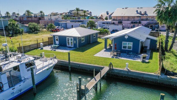 A marina with a docked boat, a small house with a blue roof, and a grassy yard.