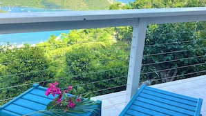 A balcony with a view of a coastal landscape, including hills and a body of water.