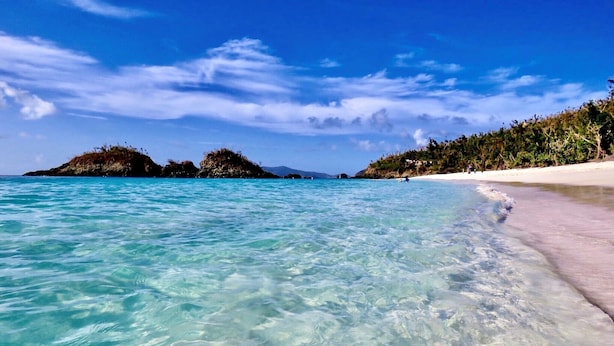 A beach with clear turquoise water, a sandy shore, and a small island in the distance.