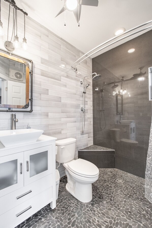 A modern bathroom with a white vanity, a toilet, a shower with a glass enclosure, and a ceiling fan.