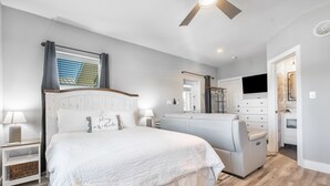 Un dormitorio con una cama grande, televisión, vestidor y baño con ducha e inodoro.