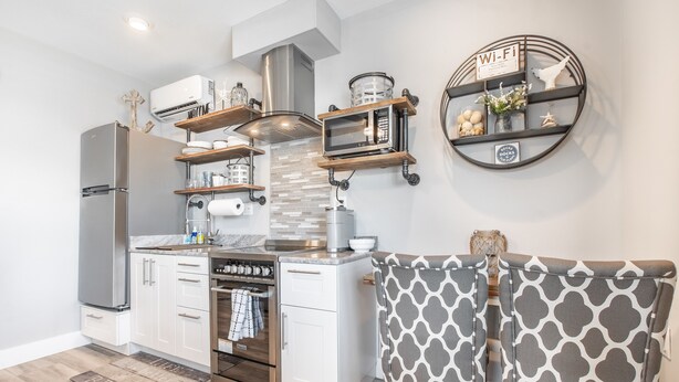 Cocina moderna con armarios blancos, un refrigerador de acero inoxidable, un horno empotrado y un microondas. Hay repisas de madera sobre la estufa y un estante redondo en la pared con un letrero de Wi-Fi.