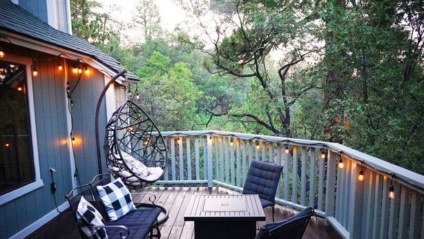 A wooden deck with outdoor furniture, string lights, and a view of a forested area.