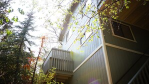 A two-story building with a balcony, surrounded by trees and foliage.